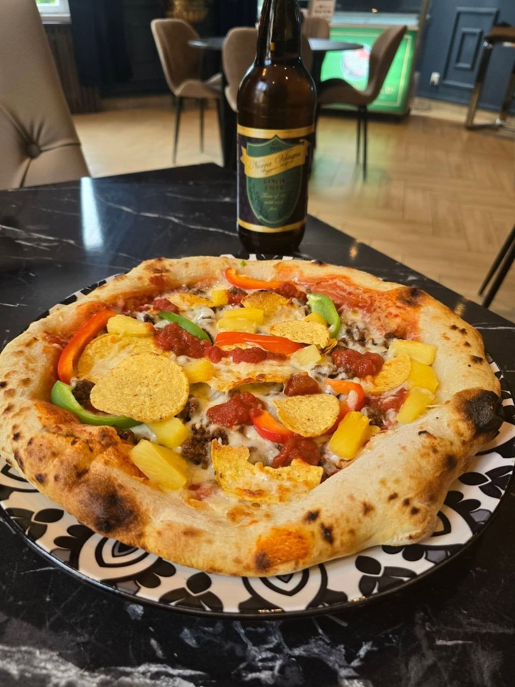 Pizza med paprika, ananas, tacofärs och nachochips på ett marmorbord i restaurangen, med en ölflaska bakom